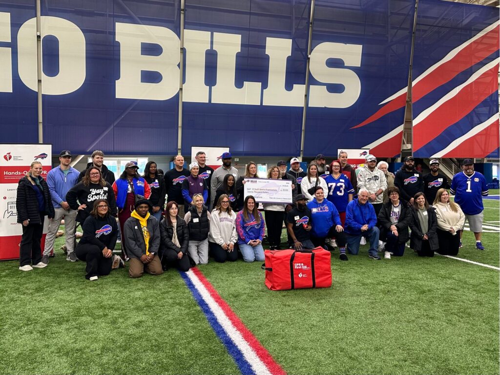 A group photo with a CPR training kit in front and two people holding a large check in the middle