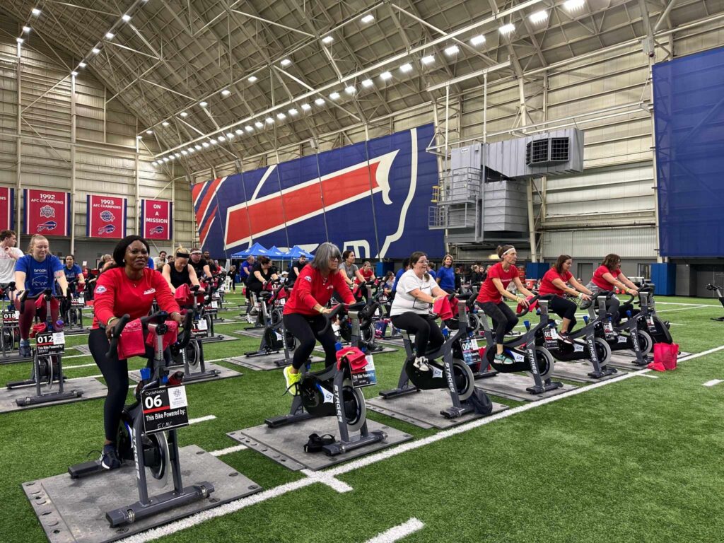 A group of people riding stationary bikes at an indoor football facility