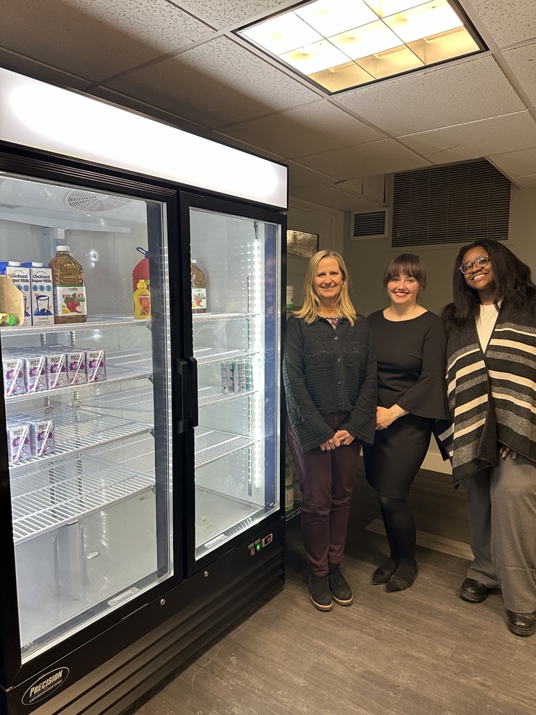 Three people stand next to a refrigerator 