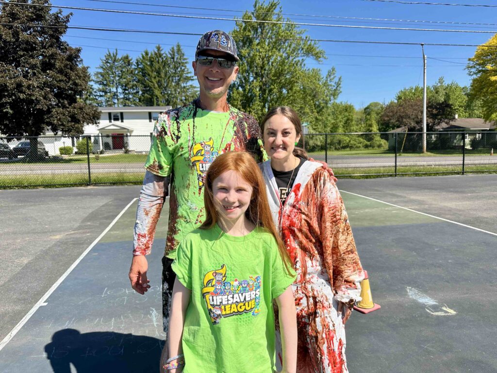 Student poses with teacher and principal covered with ice cream sundae toppings